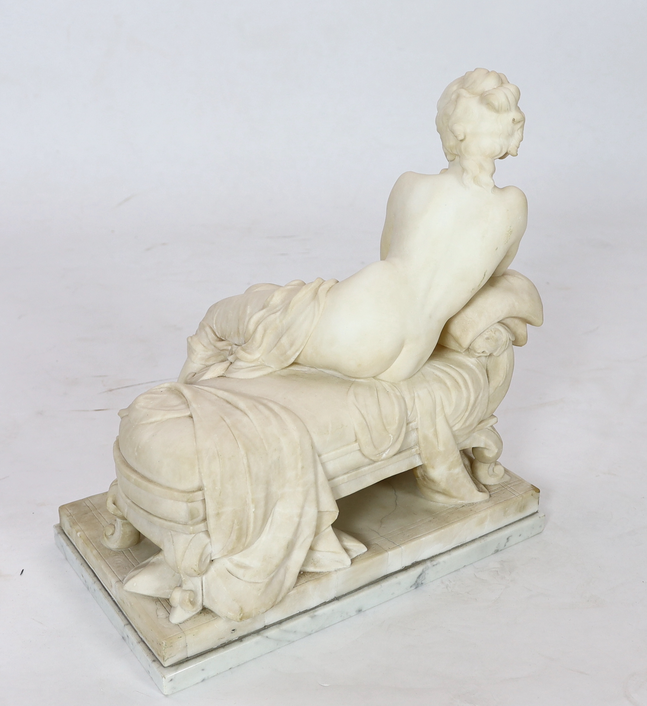 An early 20th century French carved white marble figure of a semi-clad woman seated upon a daybed, 50cm wide, 29cm deep, 52cm high